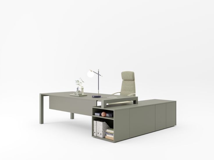 A modern L-shaped office desk in a muted gray-green color, featuring a matching high-back office chair, a desk lamp, and storage shelves with binders, set against a clean white background.